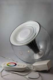 A Philips LivingColors Generation 2 light, a modern LED lamp encased in a clear, spherical shell. The lamp is placed on its side with a white remote control and power adapter beside it. The remote features a circular color wheel for adjusting the lighting hues.