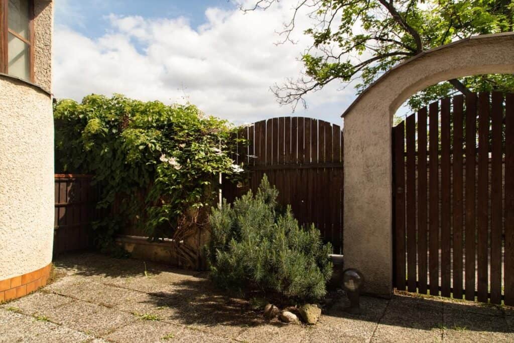 Small backyard patio area enclosed by a tall wooden fence with an arched gate and climbing greenery along the side. This shows a private and natural fencing option that works well for small spaces or garden courtyards.