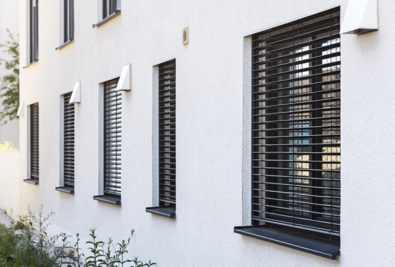 Modern white building exterior with black window shutters for privacy and style.